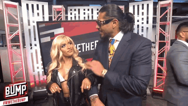 a man in a suit and tie is talking to a woman in a leather jacket in front of a bump sign