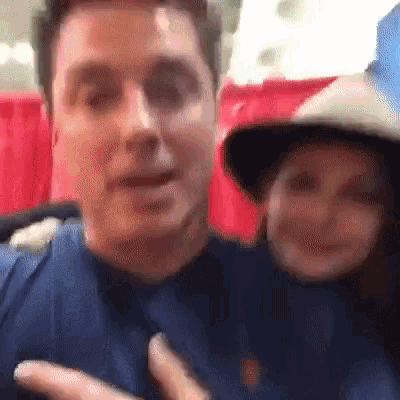 a man and a woman are posing for a picture . the man is wearing a cowboy hat .