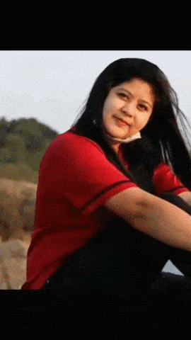 a woman in a red shirt sits on a rock with her legs crossed