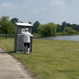 a man is running away from a portable toilet that has a sign on the door that says ' emergency exit '