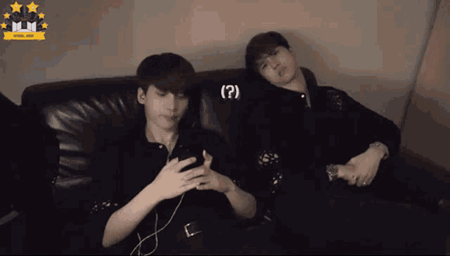 two young men are sitting on a couch looking at their phones and one of them has a question mark on his face .
