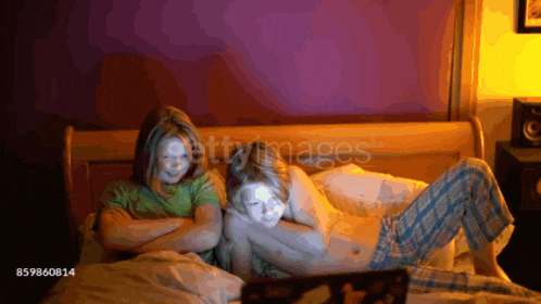 a boy and a girl are laying on a bed with their arms crossed looking at a laptop screen