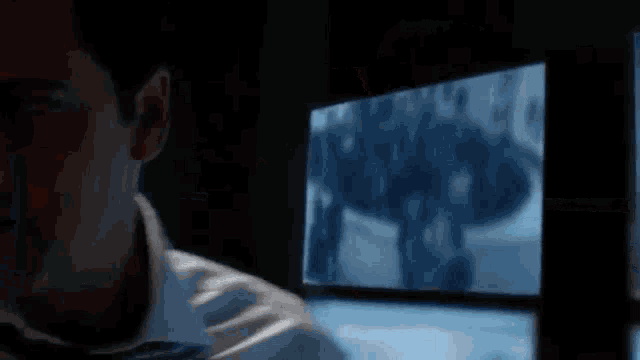 a man in a white shirt and tie is talking on a cell phone in front of a computer monitor .