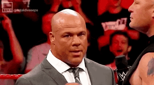 a bald man in a suit and tie is talking to another bald man in a ring .