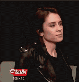 a woman wearing a black leather jacket and a black shirt is standing in front of a sign that says etalk .