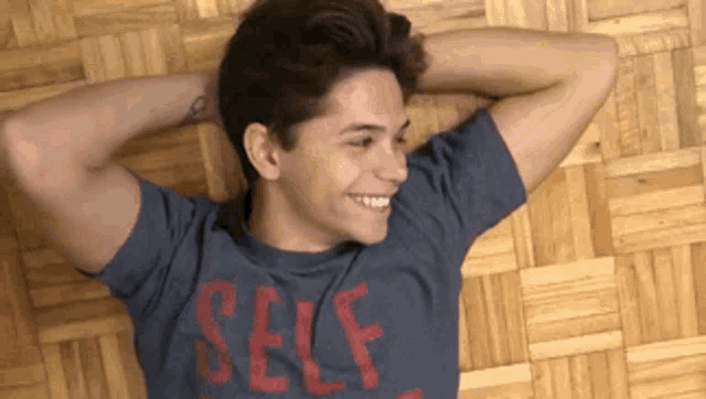 a young man is laying on the floor with his hands behind his head wearing a self shirt