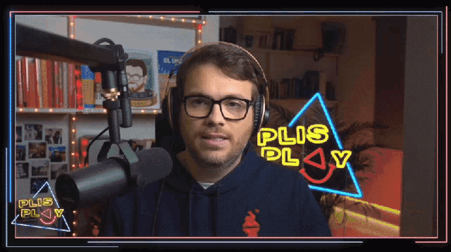 a man wearing glasses and headphones stands in front of a microphone with a neon sign that says plus play