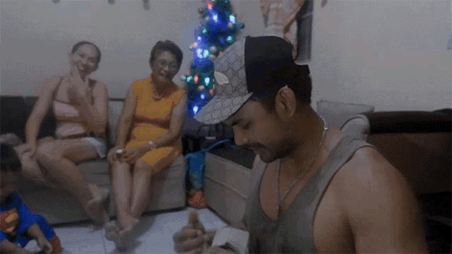 a man wearing a gucci hat sits in a living room with other people