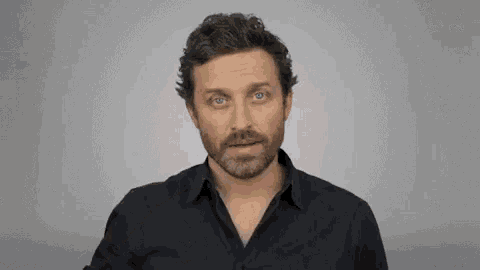 a man with a beard is wearing a black shirt and holding a cup .