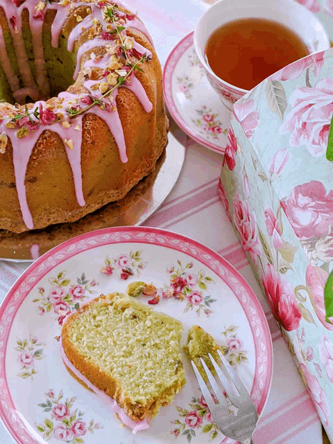 a slice of cake on a plate with a fork next to a cup of tea