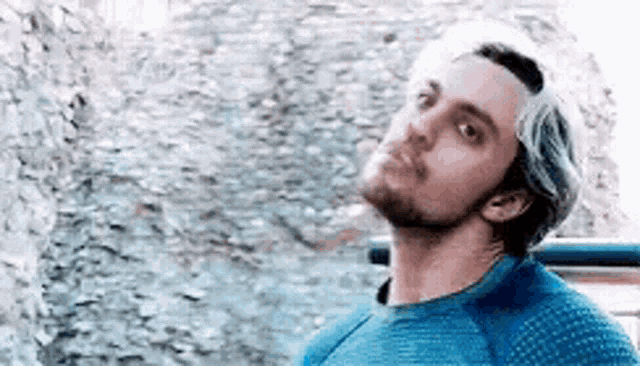 a man with white hair and a beard is wearing a blue shirt and looking up .