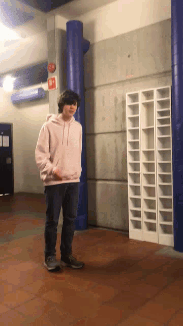 a boy in a pink hoodie stands in a hallway next to a shoe rack