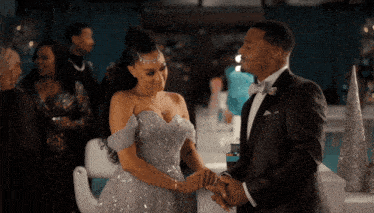 a man in a tuxedo and a woman in a ball gown are holding hands