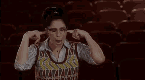 a woman with glasses is covering her ears with her hands in a theatre .