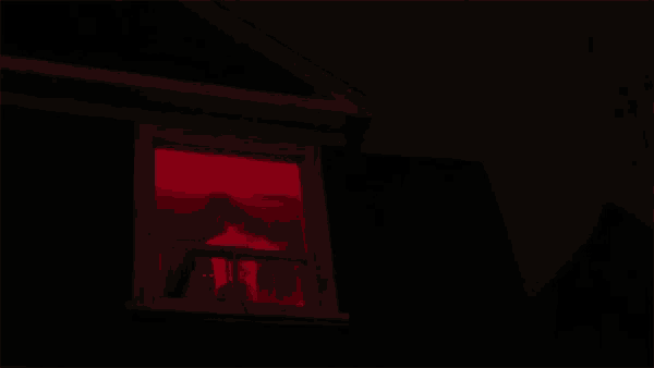 a red light is shining through a window of a dark house