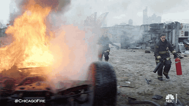 a fireman is holding a fire extinguisher in front of a burning vehicle