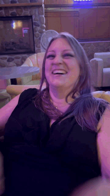 a woman in a black shirt is laughing in front of a stone fireplace