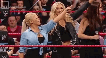 two women are standing in a wrestling ring pointing at something in the crowd .