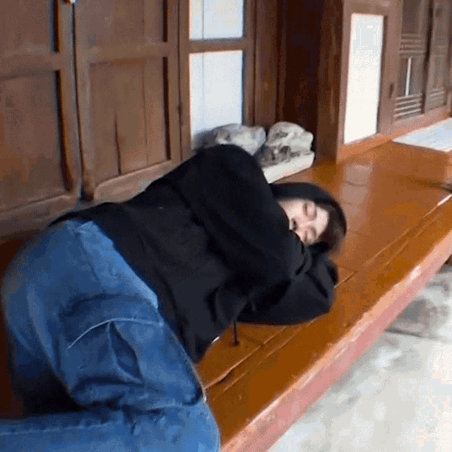 a person in a black hoodie and blue jeans is laying on a wooden bench