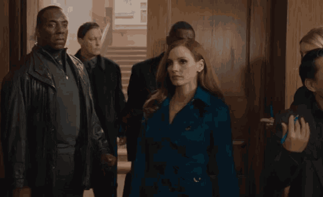 a woman in a blue coat stands in a hallway surrounded by people