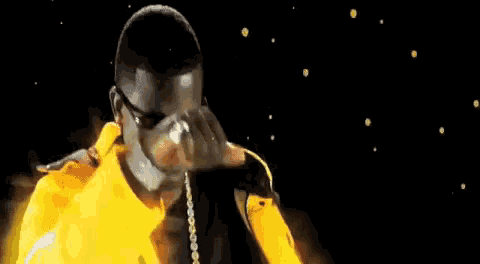a man in a yellow jacket is covering his face with his hands while standing in front of a fire .