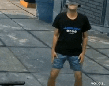 a young man wearing a black shirt and blue shorts is standing on a sidewalk .