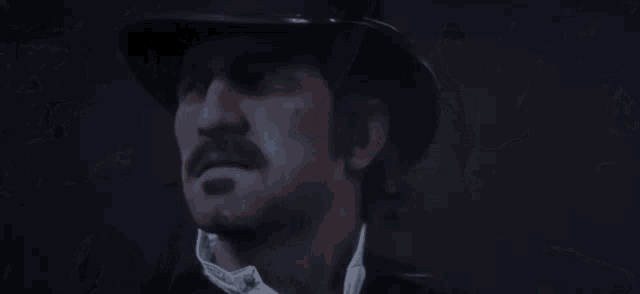 a man with a mustache and a top hat is looking at the camera in a dark room .