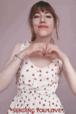 a woman in a white dress making a heart shape with her hands