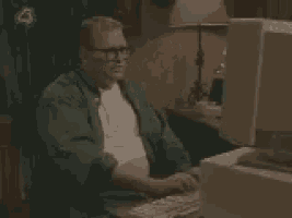 a man in a green jacket is sitting in front of a computer screen .