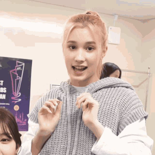 a woman wearing a grey sweater is standing in front of a poster that says ' awards ' on it