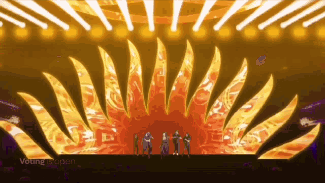 a group of people are standing on a stage in front of a large sun shaped display of lights .
