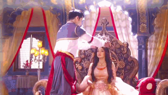 a man is putting a crown on a woman 's head while she is sitting on a throne .