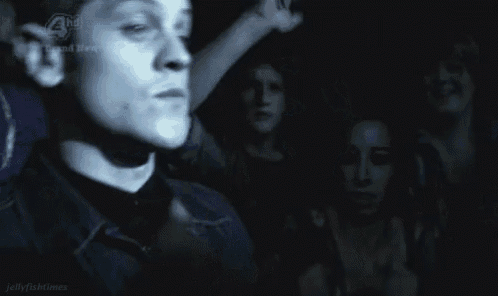 a man is standing in a dark room with his hands in the air and a crowd behind him .