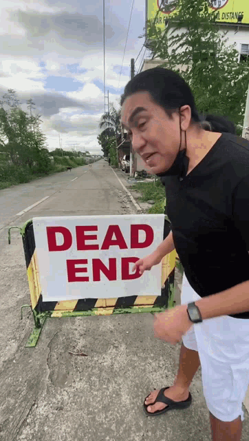a man points at a dead end sign on the side of the road