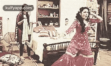 a woman in a red dress is dancing in a room while a man looks on .
