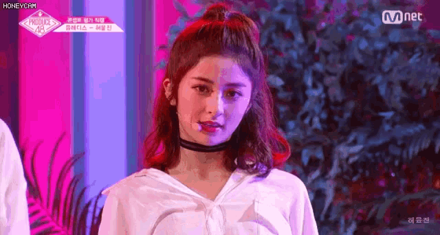 a girl with red hair and a choker around her neck is standing in front of a pink and blue background .