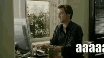 a man is typing on a computer in front of a window while drinking coffee .