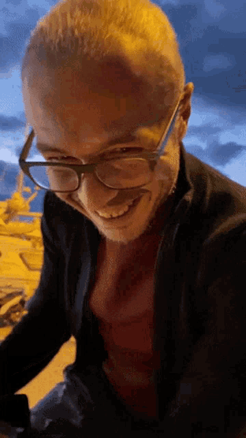 a man wearing glasses and a red shirt smiles for the camera