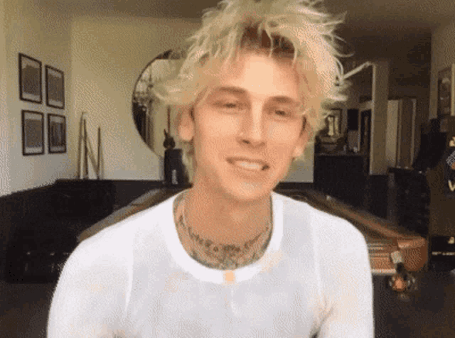 a young man with blonde hair and a tattoo on his neck is wearing a white shirt .