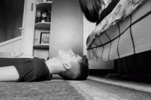 a black and white photo of a man laying on the floor with a woman standing next to him .