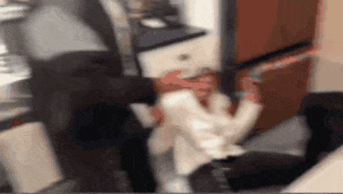 a blurry picture of a man sitting in a kitchen talking on a cell phone