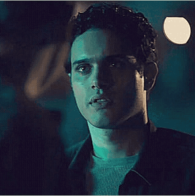 a close up of a man 's face in a dark room with a green light behind him .