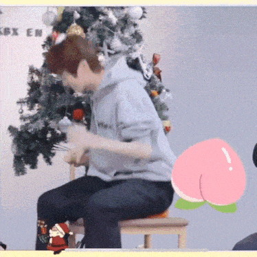 a man in a grey hoodie sits on a chair in front of a christmas tree ..