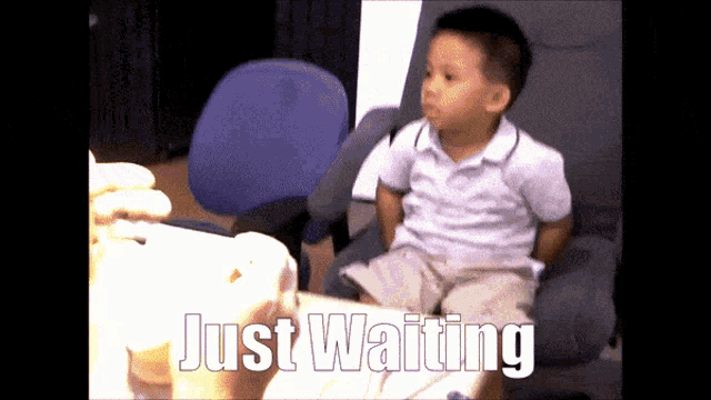 a young boy sits in a chair with the words just waiting written on the screen behind him
