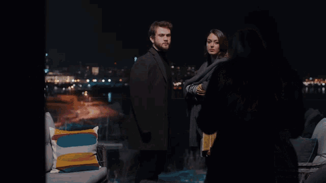 a man and two women standing next to each other on a balcony at night