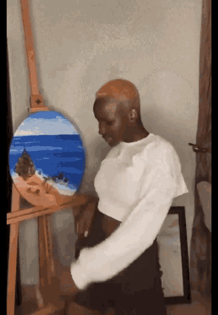 a woman is standing in front of an easel with a painting of the ocean on it