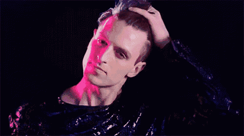 a man in a sequined sweater is touching his hair in a dark room .