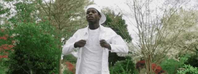 a man in a white shirt and hat is standing in a garden