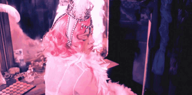 a woman with pink hair and a crown on her head looks at herself in a mirror