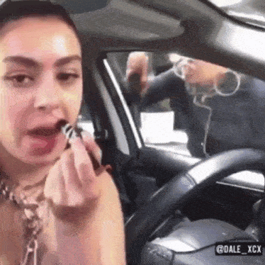 a woman is applying lipstick in a car with dale xcx written on the bottom